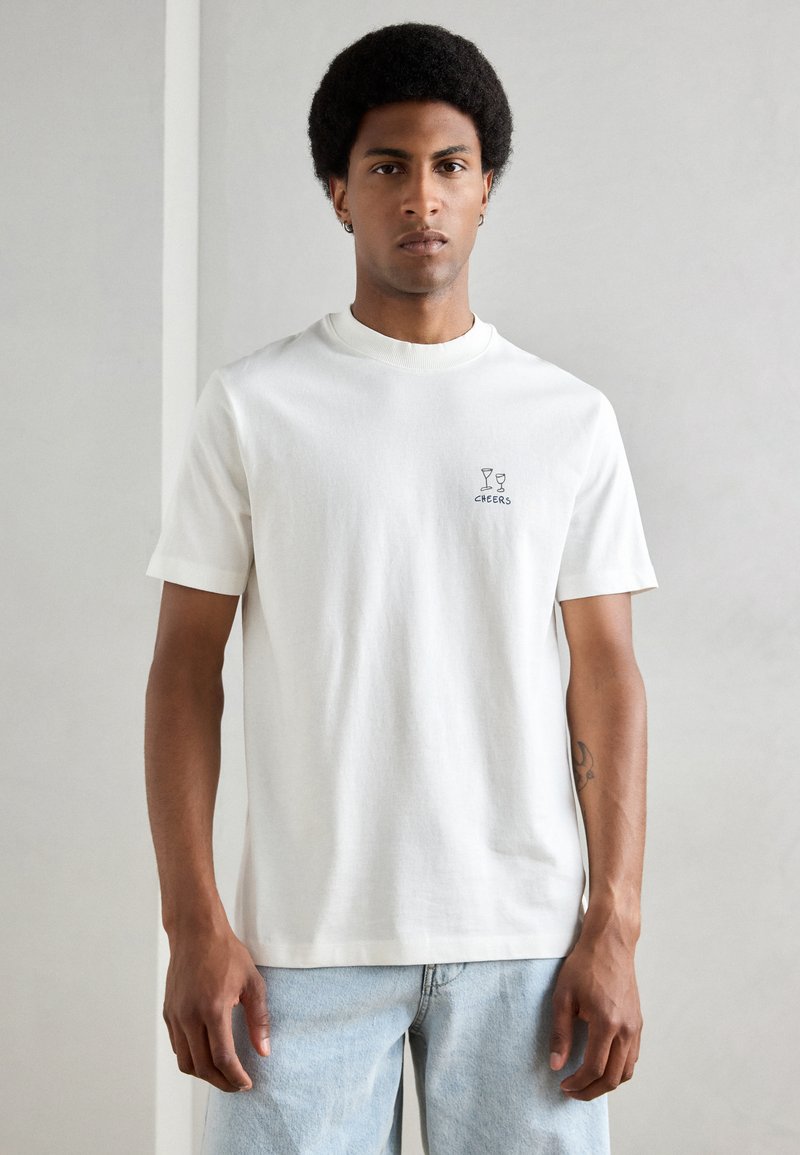 Witte katoenen T-shirt met een ribbelboordje, korte mouwen en een kleine "CHEERS" graphic met twee glazen op de linkerborst.