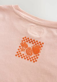 Helles pinkes Baumwoll-T-Shirt mit einem orangefarbenen Obst-Motiv in einem Schachbrettmuster auf der Rückseite, mit einem runden Ausschnitt.