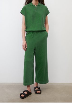 Polo verde de manga corta y pantalones de pierna ancha hechos de tela suave, con un cuello con dos botones y bolsillos laterales; sandalias negras de tipo deslizable.