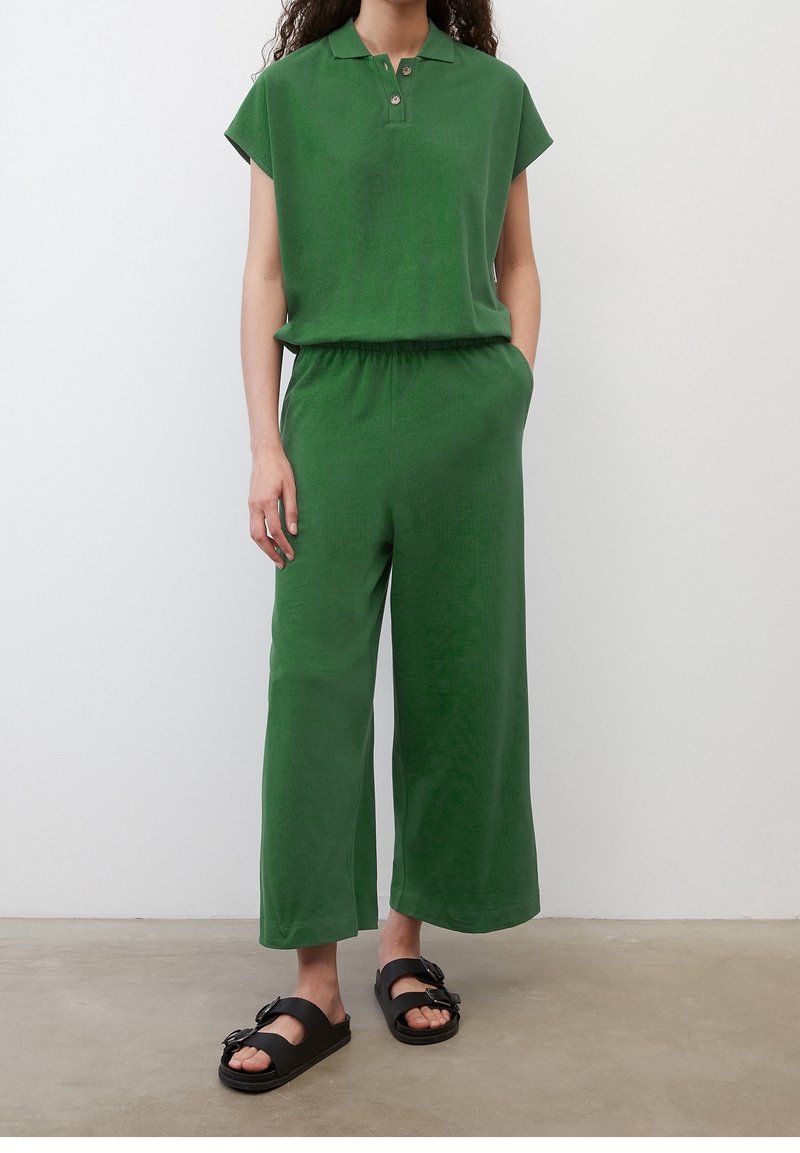 Polo vert à manches courtes et pantalon à jambes larges en tissu doux, avec un col à deux boutons et des poches latérales ; sandales plates noires.