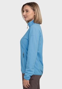 Hellblaues Fleece-Jacke mit hohem Kragen, seitlicher Reißverschlusstasche und langen Ärmeln. Weicher Stoff und minimalistisches Design ohne Muster.