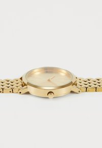 Gold metal wristwatch with a round face, smooth bezel, and a mesh band. Minimalistic design with hour markers and a single crown.