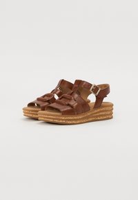 Sandali in pelle marrone con fasce larghe, dotati di dettaglio con fibbia e suola in sughero testurizzato a zeppa. Design con punta aperta per favorire la circolazione dell'aria.