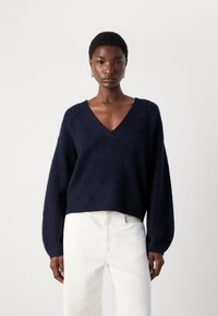 Navyblauwe, fuzzy gebreide trui met een V-hals, verlaagde schouders en lange mouwen. Gecombineerd met witte spijkerbroeken voor contrast.