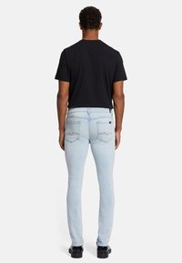 Jasnoniebieskie dopasowane dżinsy z denimu, z dwoma tylnymi kieszeniami o zaokrąglonym szwie, zestawione z czarnym t-shirtem i czarnymi butami.