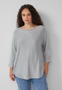 Lichtgrijze lange mouwen top met een wijde halslijn, zachte structuur en een relaxte pasvorm, met een gebogen zoom en zijsplitsingen. Gekocht in combinatie met blauwe jeans.