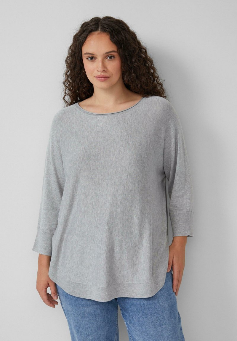 Lichtgrijze lange mouwen top met een wijde halslijn, zachte structuur en een relaxte pasvorm, met een gebogen zoom en zijsplitsingen. Gekocht in combinatie met blauwe jeans.