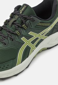 Zapatillas de running verdes con un upper texturizado y acentos en verde oscuro, detalles reflectantes y una suela blanca acolchada para mayor comodidad.