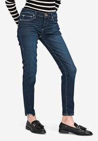 Tummansiniset farkut, kapeat lahkeet, klassisella viiden taskun muotoilulla. Varusteena vetoketju ja hienovaraiset ompeluyksityiskohdat.