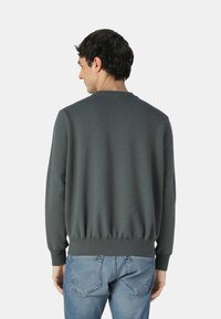 Maglione grigio scuro con collo rotondo, polsini e orlo a coste, caratterizzato da una texture sottile. Indossato sopra un paio di jeans azzurri.