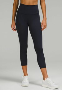 Högmidjade svarta leggings i stretchigt material, med en slät yta och kort längd, i kombination med vita sportskor.