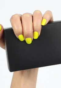 Hand with bright yellow painted nails holding a closed rectangular black box against a white background.