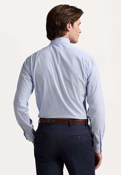 Chemise à rayures bleu clair avec un col à patte boutonnée, manches longues et coupe slim. Portée avec un pantalon sombre et une ceinture marron.