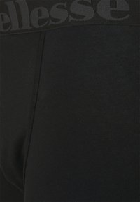 Svarta leggings med ett brett, texturerat midjeband med "ellesse"-logotypen. Materialet är slätt och elastiskt, designat för komfort och flexibilitet.