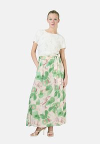 Blouse à motifs floraux blancs associée à une longue jupe fluide arborant un imprimé abstrait vert et rose, cintrée par une ceinture à nouer assortie.