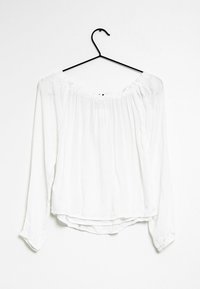 Blusa bianca a maniche lunghe con vestibilità morbida, scollatura off-shoulder, tessuto testurizzato e dettagli arricciati lungo la scollatura.