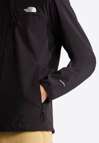 Μαύρο μπουφάν WindWall με τσέπες με φερμουάρ, ελαστικές μανσέτες και λογότυπο. Λεία υφή και εφαρμοστό σχέδιο, κατάλληλο για υπαίθρια χρήση.