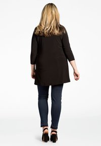 Schwarzes Tunika-Top mit 3/4-Ärmeln und geradem Schnitt, kombiniert mit dunkelblauen skinny Jeans und schwarzen High-Heels. Glatte Textur und minimalistisches Design.