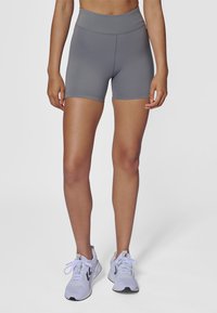 Shorts de sport gris avec une taille haute, un design élégant, des bords sans couture et une texture lisse, associés à des chaussures de course gris clair.
