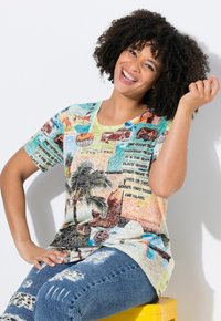 Multikleurige t-shirt met tropische print, ronde halslijn, korte mouwen, versierd met palmbomen en vintage auto's. Draagt met versleten jeans.