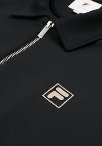 Czarna kurtka z srebrnym zamkiem błyskawicznym, spiczastym kołnierzem i kremowym, geometrycznym haftowanym logo na piersi.