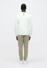 Hanorac alb cu manșete nervurate, asortat cu pantaloni de trening bej deschis și adidași albi. Un design cu dungi subtile pe partea din spate a hanoracului.