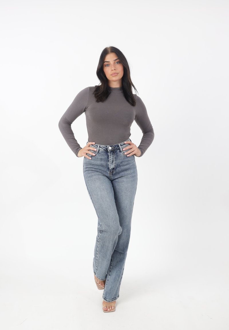 Top gris de manga larga combinado con jeans de tiro alto de color azul claro. Los jeans tienen un corte clásico y un ligero desgaste, complementados con tacones transparentes.