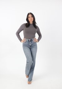 Maglietta grigia a maniche lunghe abbinata a jeans azzurri a vita alta. I jeans presentano un taglio classico e una leggera scoloritura, abbinati a tacchi trasparenti.