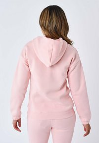 Felpa con cappuccio rosa dal taglio rilassato, con polsini e vita in costina. Tessuto liscio e design minimale senza loghi o motivi visibili.