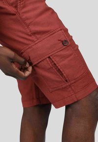 Shorts cargo rouges en tissu léger, dotés de poches latérales, d'une fermeture par bouton et de détails de couture visibles.
