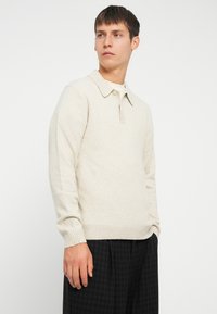 Pulóver de punto en color beige claro con cuello de punta, puños acanalados y dobladillo, con un acabado texturizado y una tapeta con un solo botón.