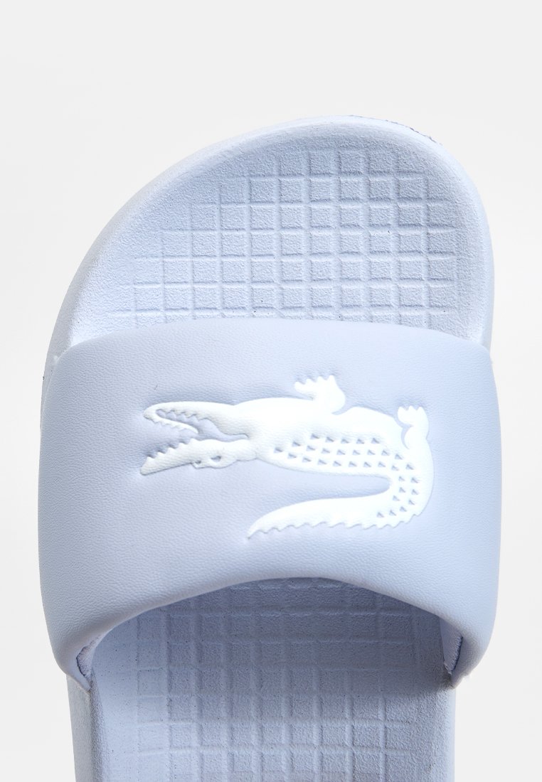 Sandale de plage bleu clair avec une semelle texturée et un logo crocodile blanc surélevé sur la sangle.