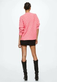 Suéter texturizado rosa con un corte amplio y mangas largas, combinado con una falda mini negra ajustada y botas negras hasta la rodilla.