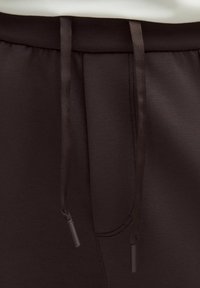 Braune Joggingshorts mit glatter Textur, Kordelzugbund mit Aglets und einer seitlichen Nahttasche für zusätzlichen Komfort.