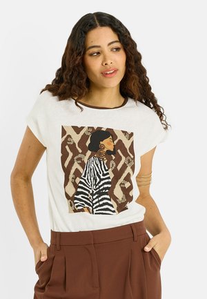 Mujer con pelo rizado que lleva una camiseta blanca con una ilustración de perfil lateral de una mujer con top de rayas de cebra sobre un fondo marrón con estampado.