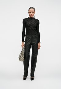 Svart langermet topp med et teksturert mønster, kombinert med høyt liv sorte bukser i kunstlær. Tilbehøret inkluderer en håndveske med slangeskinnmønster.