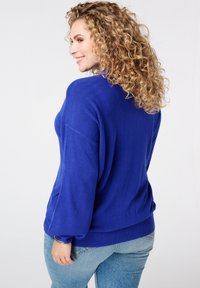 Blauwe gebreide pullovertrui met een losse pasvorm, een drapeerschouderontwerp en een geribbelde zoom. Beschikt over een zachte textuur en lange, licht ballonvormige mouwen.