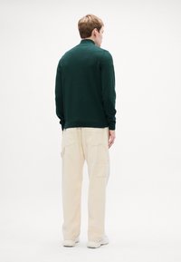 Dunkelgrüner Pullover mit Kragen, kombiniert mit cremefarbenen, lässigen Hosen mit mehreren Taschen und strukturiertem Finish. Weiße Sneakers.