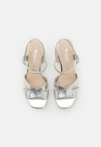 Sandalias plateadas con tacón y punta abierta, con tiras entrecruzadas y una correa ajustable en el tobillo. Talla marcada como 37. Acabado metálico suave.