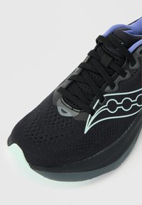 Μαύρο αθλητικό παπούτσι με αναπνεύσιμο επάνω μέρος από δίχτυ, μαύρα κορδόνια, λογότυπο ανοιχτού μπλε χρώματος και επενδεδυμένη σόλα ορατή από εμπρόσθια πλευρική γωνία.