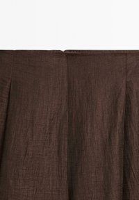 Hnědý lněný oděv s texturovaným povrchem, který má centrální zipový uzávěr na zadní straně a subtilní skladové detaily.