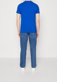 Blå kortärmad t-shirt i kombination med ljusblå jeans och vita sneakers, sedd bakifrån. Mjuk tyg och avslappnad passform.