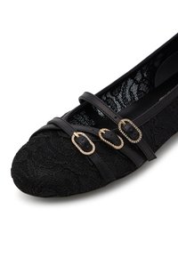 Ballerine nere con sovrapposizione di pizzo, tre cinturini decorativi con dettagli in oro e punta arrotondata.