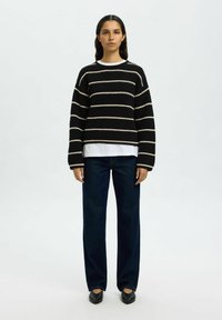 Maglione a strisce bianche e nere lavorato a maglia con maniche ampie, abbinato a jeans dritti scuri e scarpe nere. Look stratificato semplice.