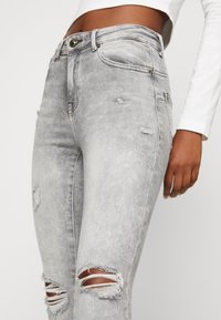 Jeans skinny desgastados en gris con roturas en las rodillas, que cuentan con una cintura alta y una sutil textura stone-washed.