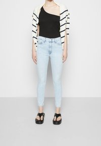 Czarny bodysuit na jedno ramię, jasnoniebieskie dżinsy z wysokim stanem i czarne klapki. Lekki, prążkowany kardigan narzucony na ramiona.