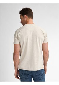 Camiseta de algodón beige con cuello redondo, mangas cortas y corte relajado, combinada con jeans de mezclilla azul que presentan costuras en los bolsillos traseros.