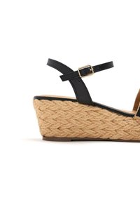 Sandalía de cuña negra con tiras, con una plataforma de yute trenzado. El tacón presenta un patrón de trenzado texturizado y una correa ajustable con hebilla.