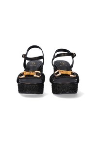 Las sandalias de plataforma negras presentan una textura trenzada y una parte superior suave. Los acentos en tono dorado y un detalle de hebilla son prominentes.