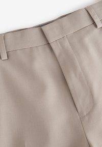 Beżowe spodnie o gładkiej teksturze materiału, z paskiem w talii i prostym fasonem z przodu. Minimalne przeszycia podkreślają eleganckie wykończenie.